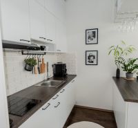 A kitchen in a 2-room apartment with a white brick wall and a wooden decor floor.