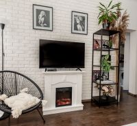 Living room with a white brick wall, decorative fireplace, black armchair, and wood-patterned flooring.