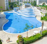A pool in Iskele surrounded by palm trees and loungers near apartment buildings.