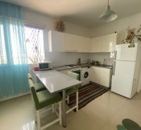 A one-room apartment kitchen with a window, appliances, and light-colored furniture.