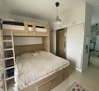 A space in a studio apartment with a bunk bed, built-in wardrobe, and floral curtains.