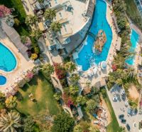 Aerial view of pools and gardens in the city of Iskele, surrounded by greenery and buildings.