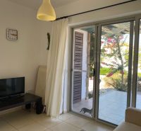 Living room of a two-room apartment with a television, curtains, and sliding doors to the terrace.