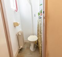 A toilet with a toilet bowl, radiator, and floor with wood decor in a 2-room apartment.