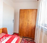 A room with a wooden wardrobe, a bed, and a red carpet in a 2-room apartment.