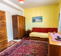A room in a two-room apartment with wooden furniture and a red carpet.