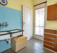 A kitchen in a 2-room apartment with blue tiles and wooden decor furniture.