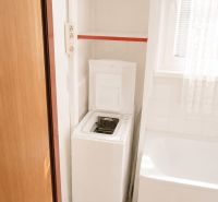 Bathroom in a 3-room apartment with a washing machine, bathtub, and shelves.