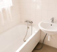 A bathroom with a bathtub and a sink in a 3-room apartment. Light tiles on the walls.