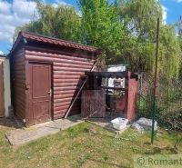 A wooden cottage in Holíč surrounded by greenery and a fence under a blue sky.