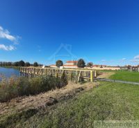 A lake with an elevated wooden pier in Holíč, next to it grass and a beach.