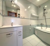 A bathroom with light tiles and a hanging bathtub in a 3-room apartment.