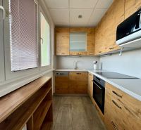 A kitchen in a 3-room apartment with a kitchen unit, wooden decor flooring, and large windows.