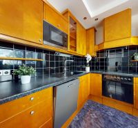 A kitchen with yellow-brown cabinets, black tiles, built-in appliances, plants, 4-room apartment.