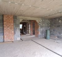 An incomplete wall in a family house made of bricks and concrete, without flooring finishes.