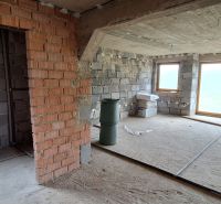 An unfinished interior of a family house with unplastered brick walls and large windows.