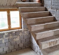 A staircase in an unfinished family house with gray bricks and a wooden window.