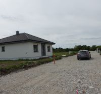 A family house in Reca with a car on a gravel access road and a garden.
