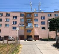 Brick building in Moravské Lieskové, a place for a 3-room apartment, surroundings with cars and trees.
