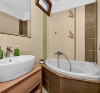 Bathroom with a corner bathtub and a sink in a 3-room apartment, beige tiles.