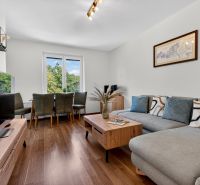 A bright living room in a three-room apartment with a wooden decor floor and a sofa.