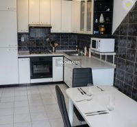 A kitchen with white cabinets in a 3-room apartment, a dining table, and ceramic tiles.