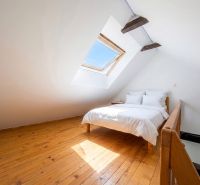 Attic bedroom with a bed and a skylight, wooden decor flooring.