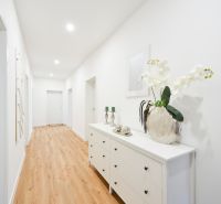 A hallway in a family house with white furniture and a wooden-patterned floor.