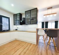 A kitchen in a family house with white cabinets, a bar counter, and a wooden decor floor.