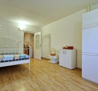 A bedroom in a 2-room apartment with white furniture and a wood-patterned floor.