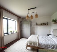 A bedroom in a cottage with a comfortable bed, an open window, and decorations on the shelves.