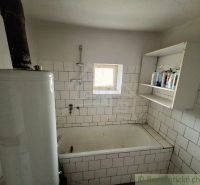 Bathroom in a cottage with tiles, a bathtub, and shelves for toiletries.