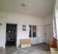 The interior of a cabin with worn walls, older furniture, and a radiator under the window.