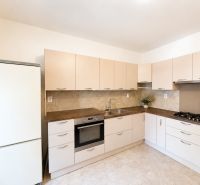 A kitchen with beige cabinets and appliances in a three-room apartment, flooring with a wood decor.