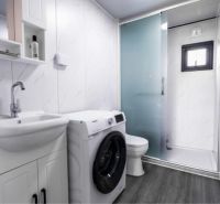 Bathroom with a washing machine in a family house, white cabinets, glass shower, and mirror.