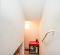 A staircase leading to the basement in a family house, illuminated by a window, with storage spaces inside.