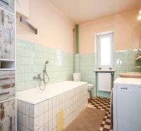 A bathroom in a family house with a bathtub, washing machine, tiles, and cabinets with wood decor.