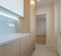 A narrow kitchen with light cabinets that frame the entrance to another room.