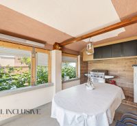 A covered terrace with a grill in a family house, surrounded by greenery.