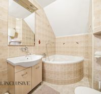A bathroom with light tiles, a corner bathtub, and a sink in a family house.
