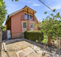 A family house in Gabčíkovo with a pink facade, a balcony, and a garden, surrounded by greenery.
