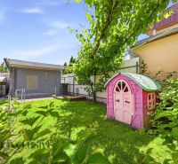 The courtyard of a family house in Gabčíkovo with a children's playhouse and a pergola, surrounded by greenery.
