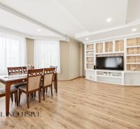 A dining room with a wood-patterned floor and a TV wall in a family house.