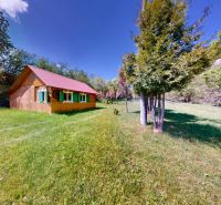 A cottage in Poráč with a red roof surrounded by greenery and trees on a vast meadow.