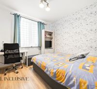A bedroom with a desk, chair, brick wallpaper, and a wooden decor floor in a 3-room apartment.