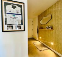 A hallway in a 3-room apartment with a mirror, lighting, and a football jersey on the wall.