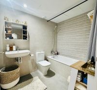 A bathroom in a 3-room apartment with a bathtub, sink, toilet, and light tiles.