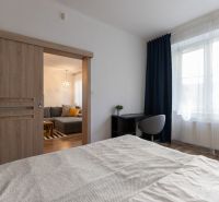 Bedroom with glass doors in a 2-room apartment, work desk, wooden decor flooring.