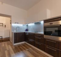 A kitchen in a 2-room apartment with dark furniture and a wooden decor floor.
