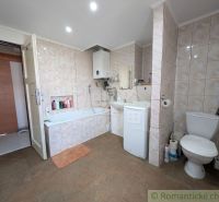 Bathroom in a 2-room apartment with a bathtub and a washing machine, tiled with light tiles.